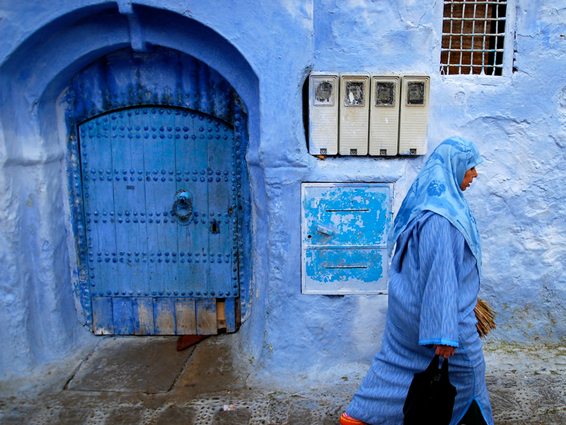 A lady captured walking in front of a blue house in Morocco. (Pic credit: Roy Cheung/Flickr)