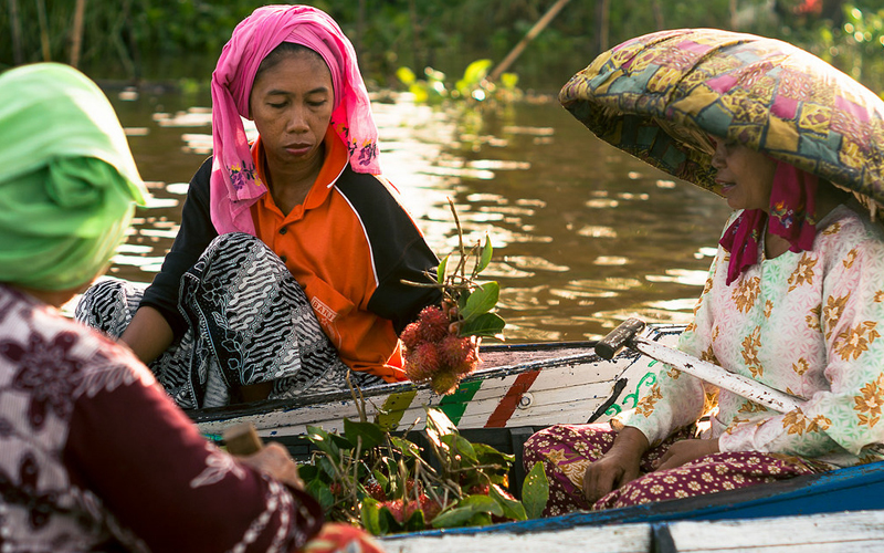 A woman considers a bunch of rambutan fruit, at the Lok Baintan floating market near Banjarmasin, Indonesia. (Photo credit: killerturnip/Flickr) 