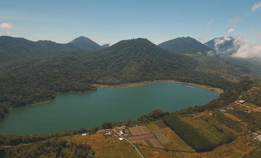 Quiet view of Lake Tamblingan in northern Bali, Indonesia, with misty mountain slopes and lush green rainforest along the shore.