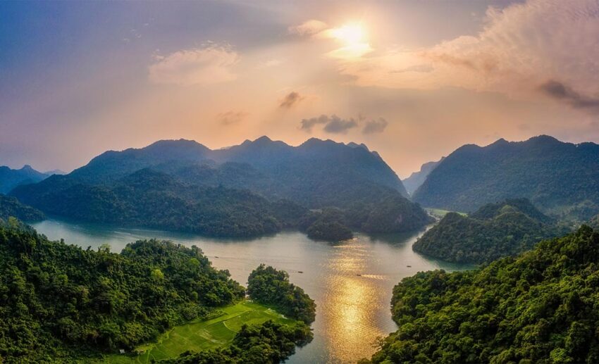Serene spring landscape of Ba Be Lake in Vietnam, featuring calm freshwater surrounded by misty limestone mountains and forest.