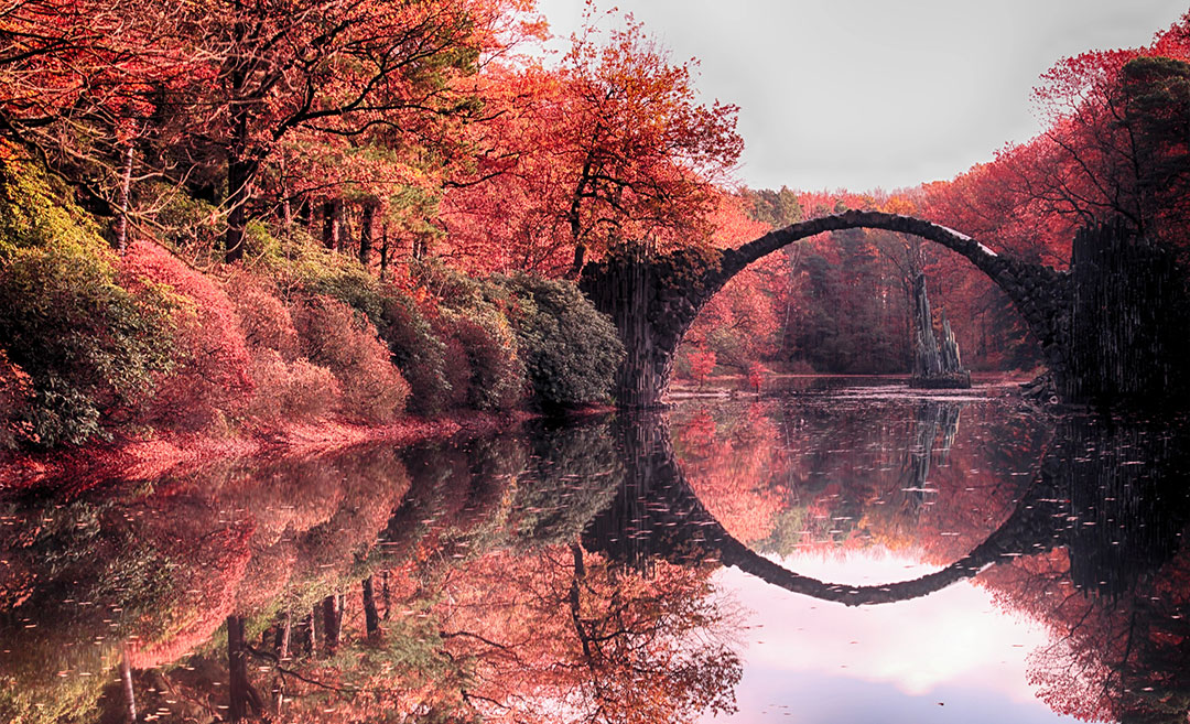 semi-circular stone arch of Rakotz Bridge, reflecting perfectly on the still water, forming a complete, mesmerising circle.
