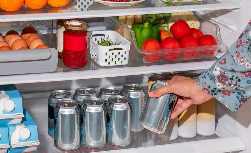 Person reaching inside a well-stocked and open refrigerator filled with fresh food and drinks