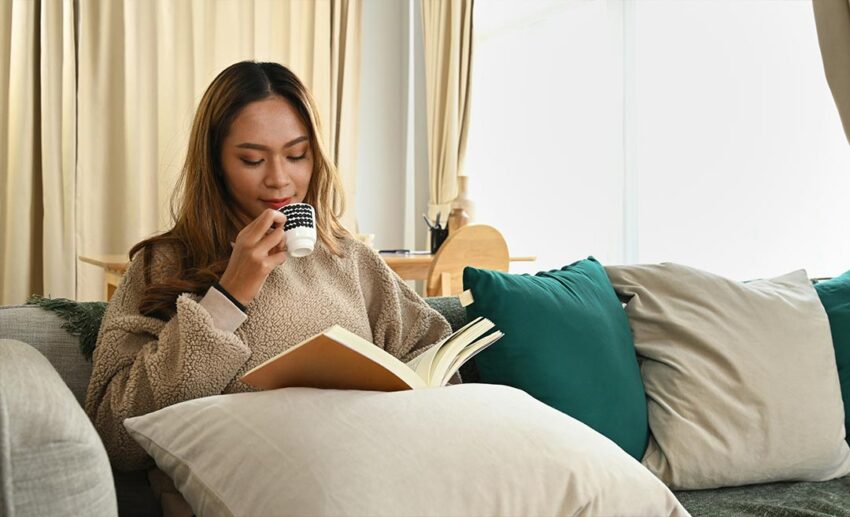 Woman relaxing peacefully on a sofa indoors reading a book with a mug in hand
