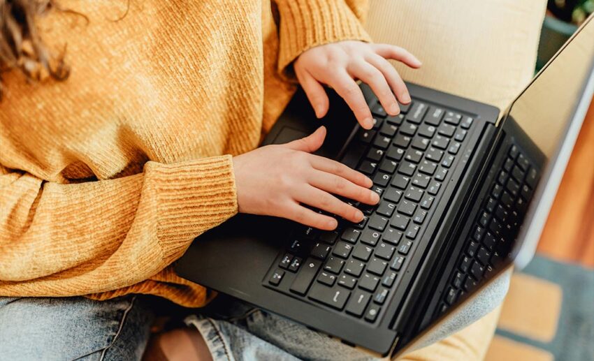 Close-up of a woman sitting on a couch while comparing flight options on her laptop computer.