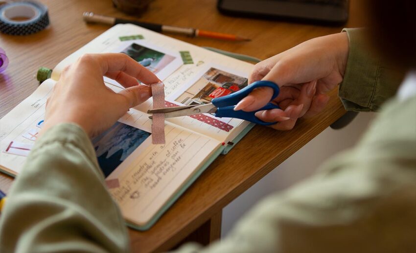 Close-up of a person using washi tape for a travel journal, demonstrating analogue documenting to reclaim travel joy.