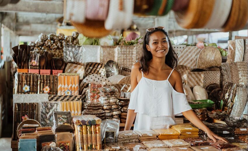 A woman smiling in a local handicraft store surrounded by spice packets and woven baskets, supporting local heritage.