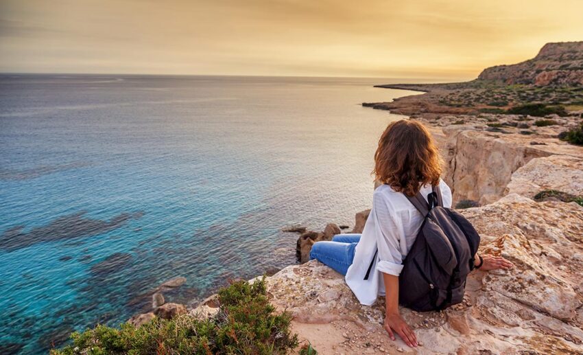 Woman sitting on a cliff overlooking the ocean at sunset for a reflective evening.