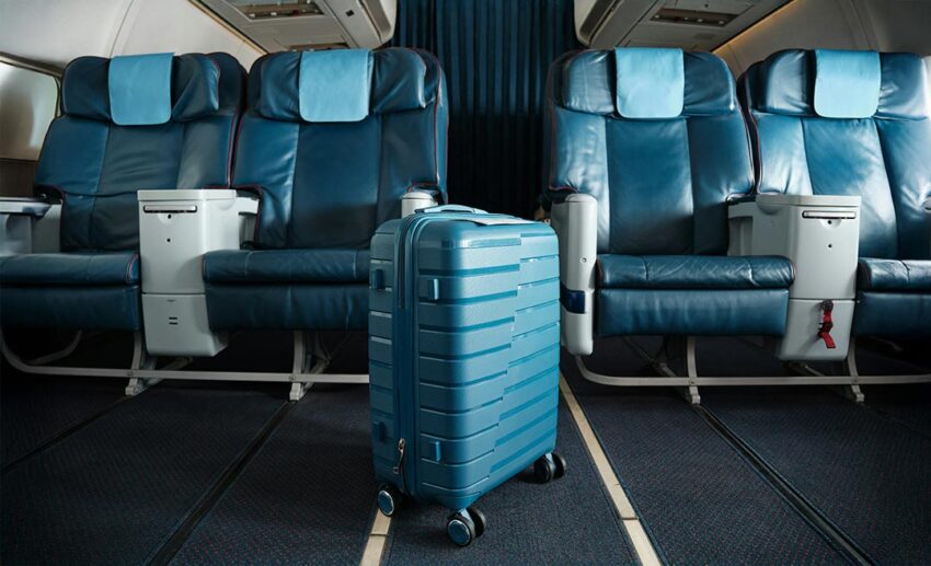 Blue cabin-sized roller bag standing upright in the aisle between airplane seats.