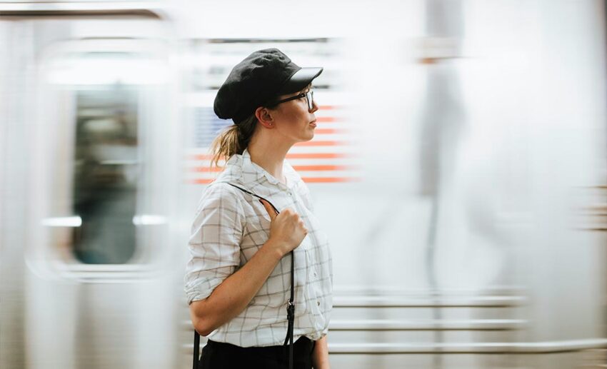 A woman in a hat and glasses standing by a moving train, choosing local transit over viral tourist traps to avoid travel burnout.