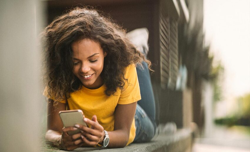 A woman smiling at her mobile phone while relaxing on an outdoor bench, representing the balance of social media and travel joy.