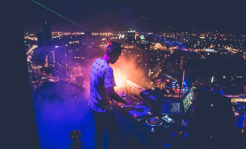 DJ playing music at a rooftop bar during an upbeat evening social event.