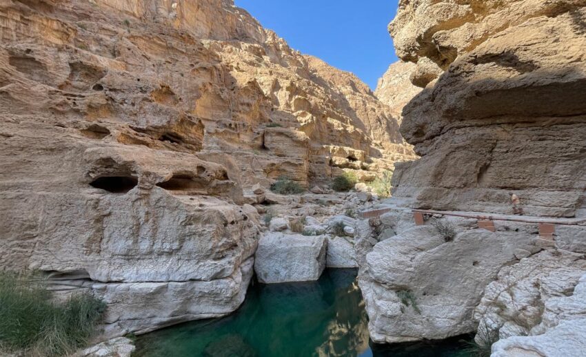 A view of the emerald water and rock formations inside Wadi Shab, Oman, showing the natural river valley oasis.