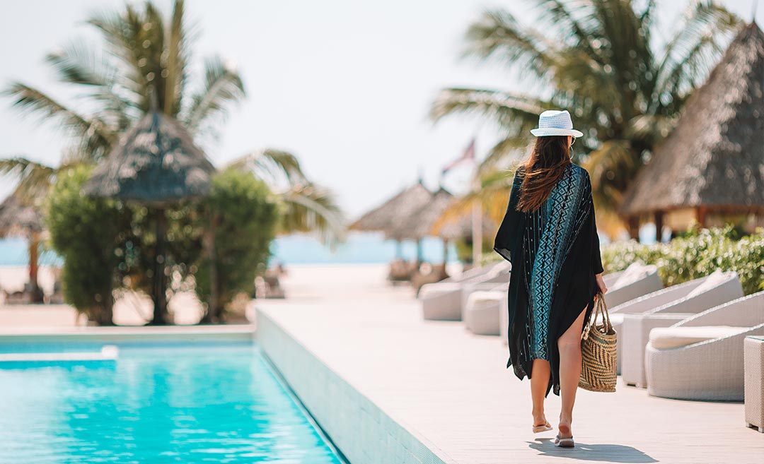 Woman in summer vacation attire walking by a luxury swimming pool, representing mindful travel planning.