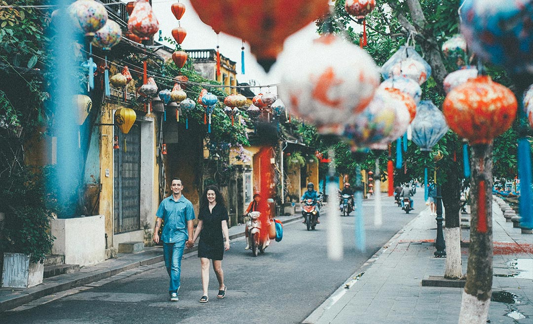 couple exploring a lantern-decorated street in Southeast Asia with motorbikes, illustrating multi-city travel with the Emirates Asia Pass.
