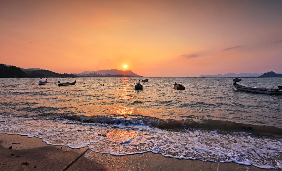 Traditional wooden fishing boats at sunset on a Langkawi beach, a top destination for Visit Malaysia 2026.