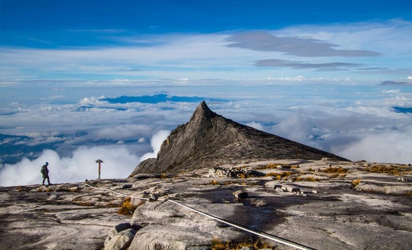 Hiker walking toward South Peak at Mount Kinabalu in Sabah, Borneo, above the clouds at sunrise.