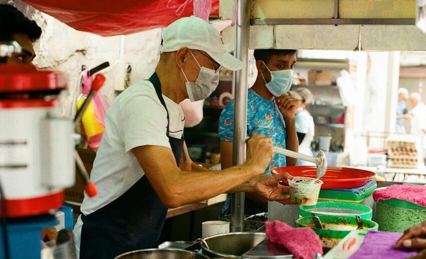 A Penang hawker stall seller packing a takeaway container of cendol, representing Malaysia’s famous street food culture.