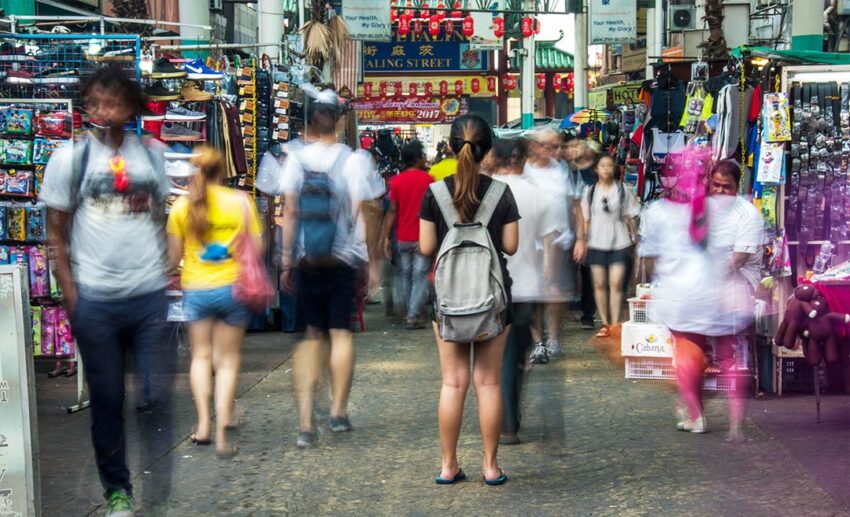 Long exposure of a female traveller with a backpack in Petaling Street, Kuala Lumpur, highlighting the city's vibrant layers.