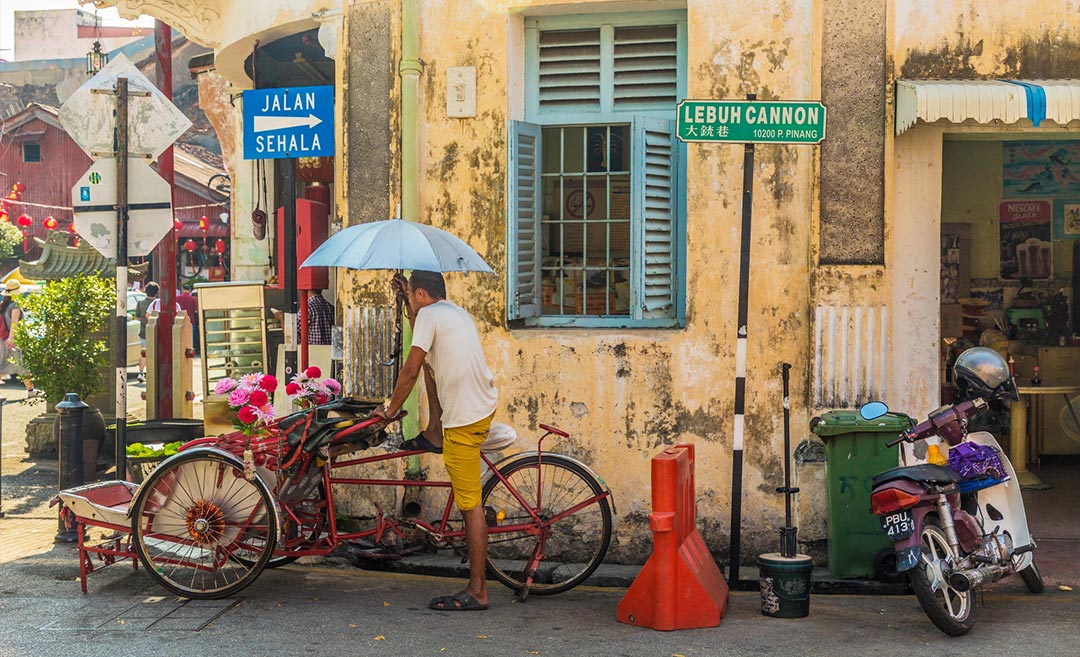 A traditional trishaw rider parked along the historic Lebuh Cannon in Penang, showcasing heritage architecture and local backyard travel.
