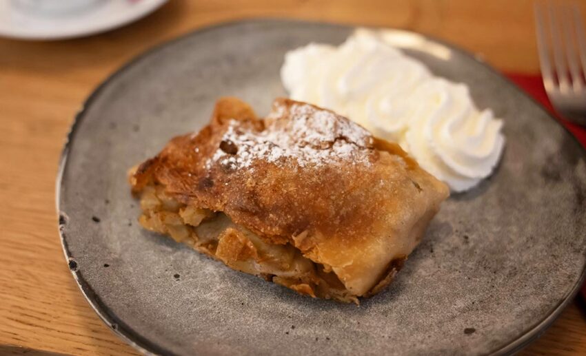 A slice of traditional Austrian Apfelstrudel (apple strudel) served with a side of fresh whipped cream at a local Vienna kaffeehaus.