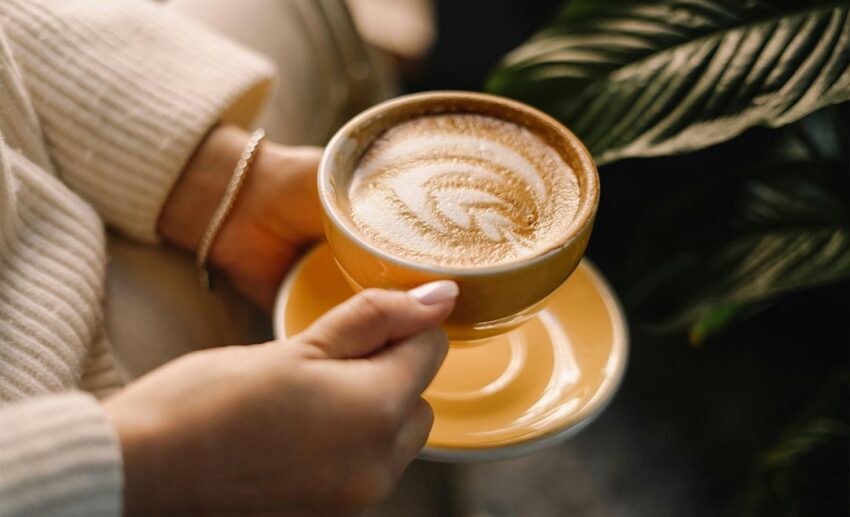 Close-up of a person's hands holding a cup of hot coffee with latte art, illustrating high coffee consumption in Austrian culture.