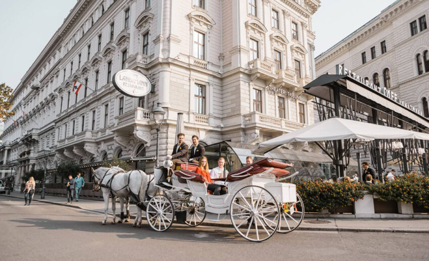 Smiling passengers in a traditional white horse-drawn Fiaker carriage touring the historic city centre of Vienna.
