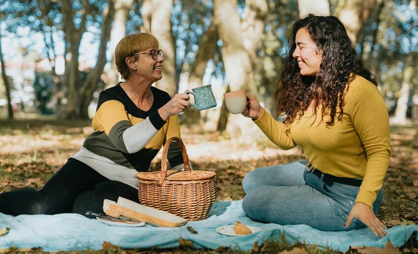 An adult daughter and her mother sitting together on a picnic blanket in a quiet park, sharing a moment of reconnection.