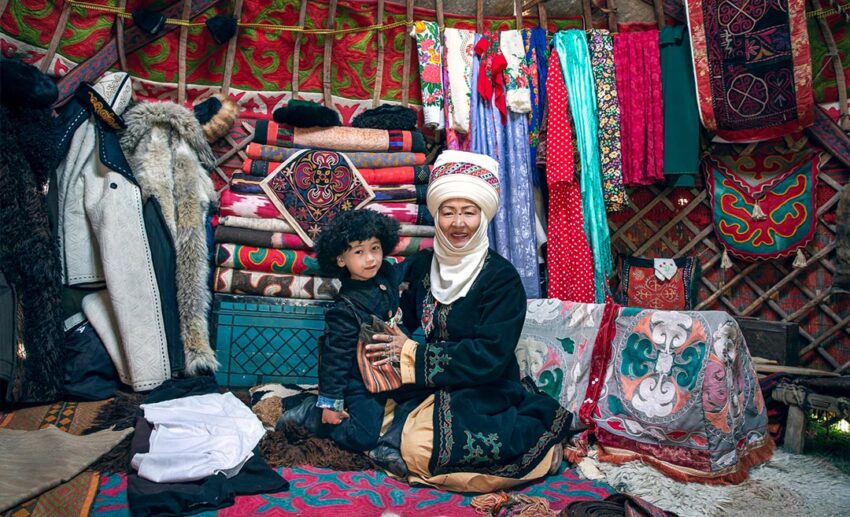 A Kyrgyz mother and her son wearing traditional Kyrgyz dress inside a beautifully decorated yurt.
