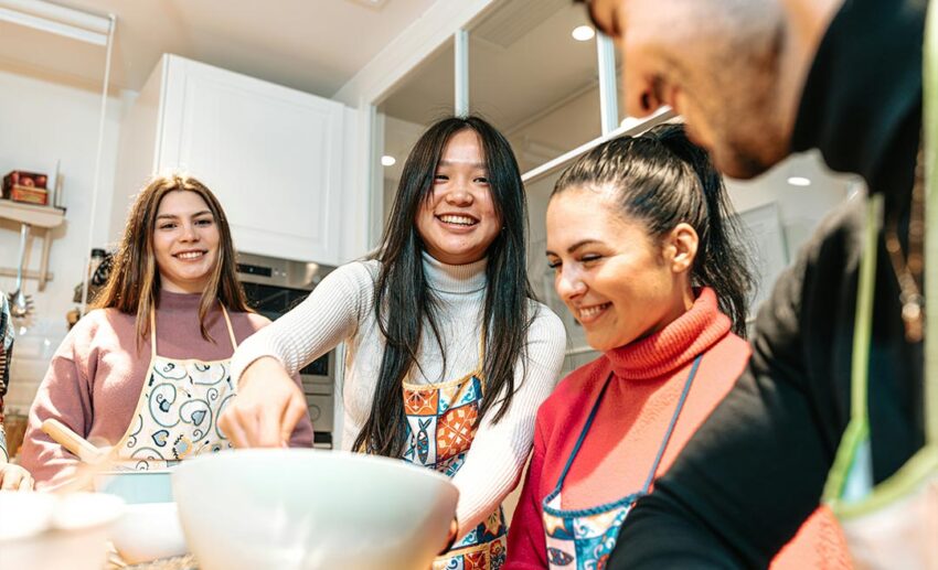 A group of close friends laughing while preparing food together during a professional cooking class retreat.