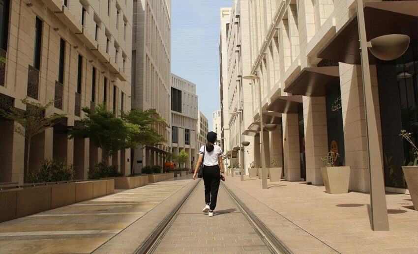 A woman walking confidently through the modern, sustainable architecture of Msheireb Downtown Doha during a stopover.