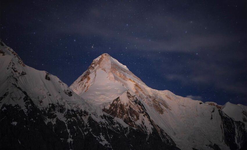 A dramatic view of snow-capped Tian Shan mountain peaks under a clear, starry night sky in Central Asia.