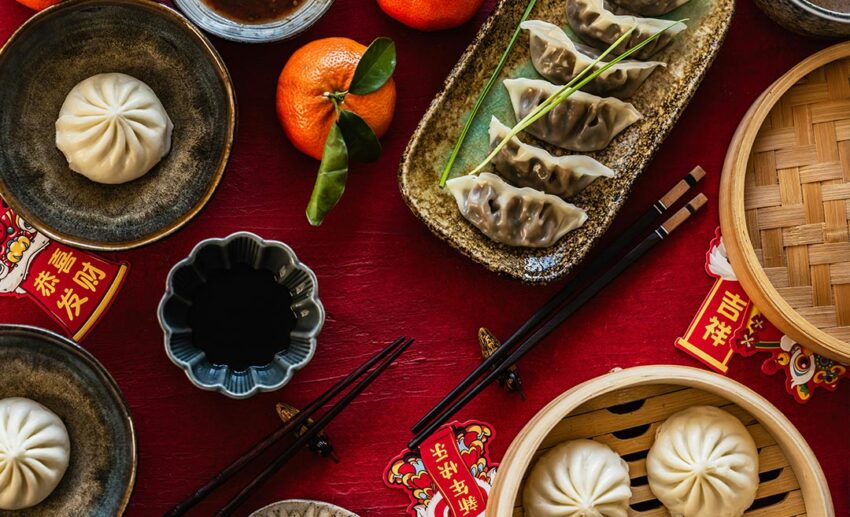 Overhead shot of a red-clothed table with steamed paos, dumplings, and oranges as offerings for the Chinese God of War, Guan Yu.