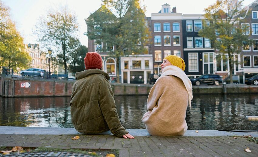 A back view of two women deep in conversation while sitting by an Amsterdam-style river canal.