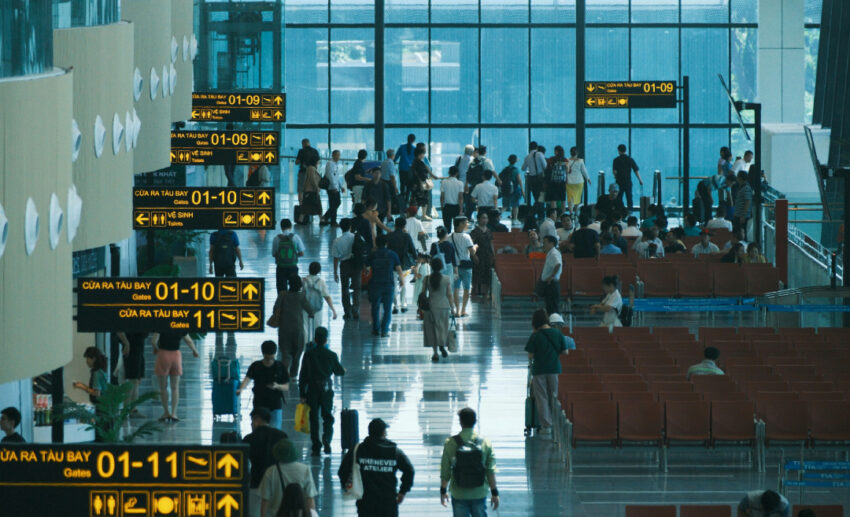 A busy international airport terminal with travellers and flight information displays, highlighting the risk of airborne diseases in high-traffic transport hubs.
