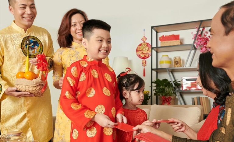 A multi-generational Chinese family participating in the traditional Bai Nian greeting; children in traditional attire receive red envelopes (ang pao) from their grandparents.