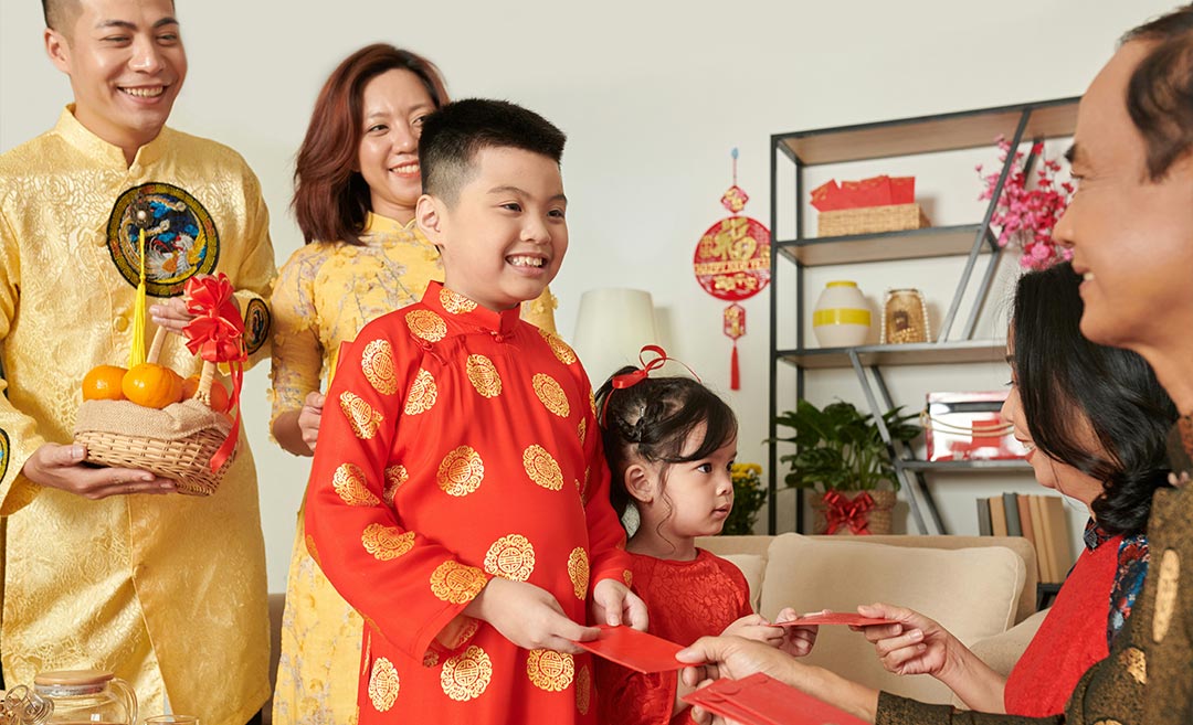 A multi-generational Chinese family participating in the traditional Bai Nian greeting; children in traditional attire receive red envelopes (ang pao) from their grandparents.