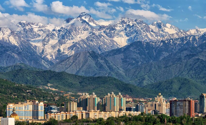 The snow-capped peaks of the Zailiysky Alatau mountain range towering over the modern city skyline of Almaty, Kazakhstan.