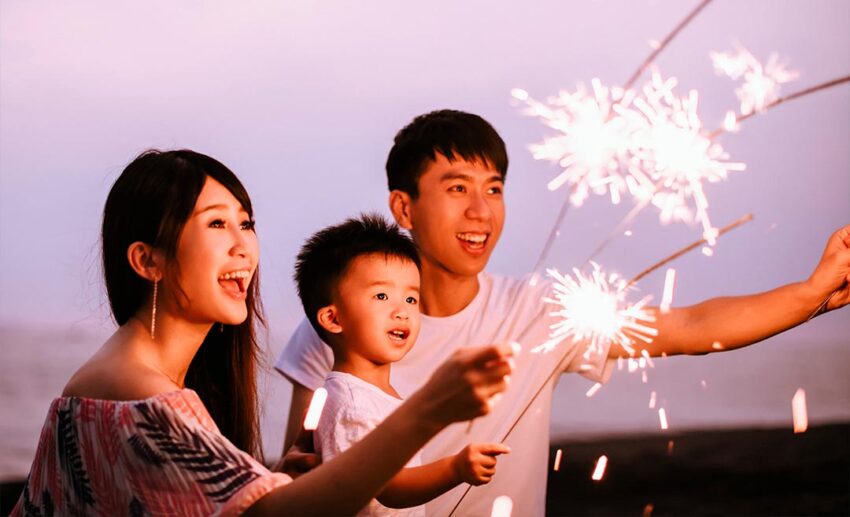 A mother, father, and son dressed in festive red outfits playing with sparklers to celebrate the first day of the Lunar New Year.