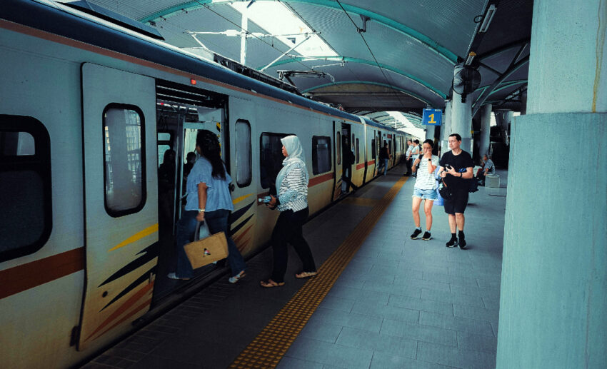 Commuters boarding and disembarking a KTM Komuter train at a station in Malaysia, illustrating the importance of ventilation in public transport.