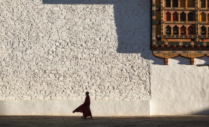 A Buddhist monk walking through the sunlit courtyard of Rinpung Dzong, also known as Paro Dzong, in Bhutan.