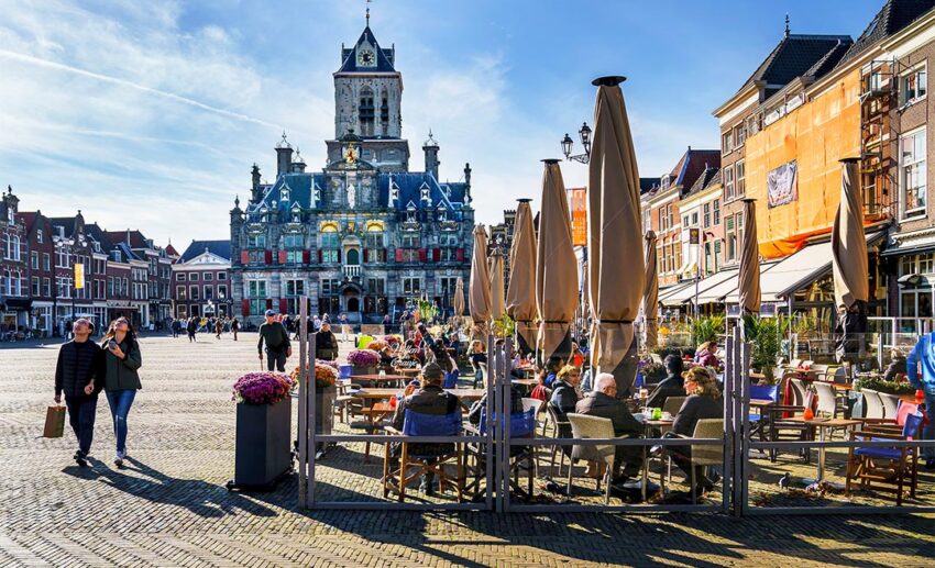 Locals and visitors gathered at open-air cafes in Delft’s vast Markt square, with the historic Renaissance Town Hall serving as a backdrop under the afternoon sun.