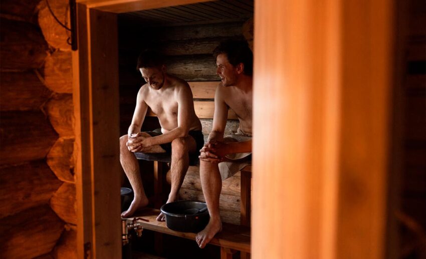 Two men sitting on wooden benches inside a traditional Finnish wood-heated sauna in Hamina.