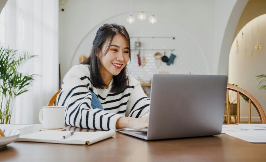 A young Asian female student focused on her laptop at home, representing the simple online process of checking FLYsiswa eligibility through the Ministry of Transport portal.