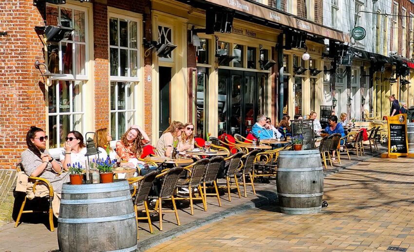 The lively Beestenmarkt square at dusk, showing crowded outdoor restaurant tables and a social, relaxed atmosphere under the trees.