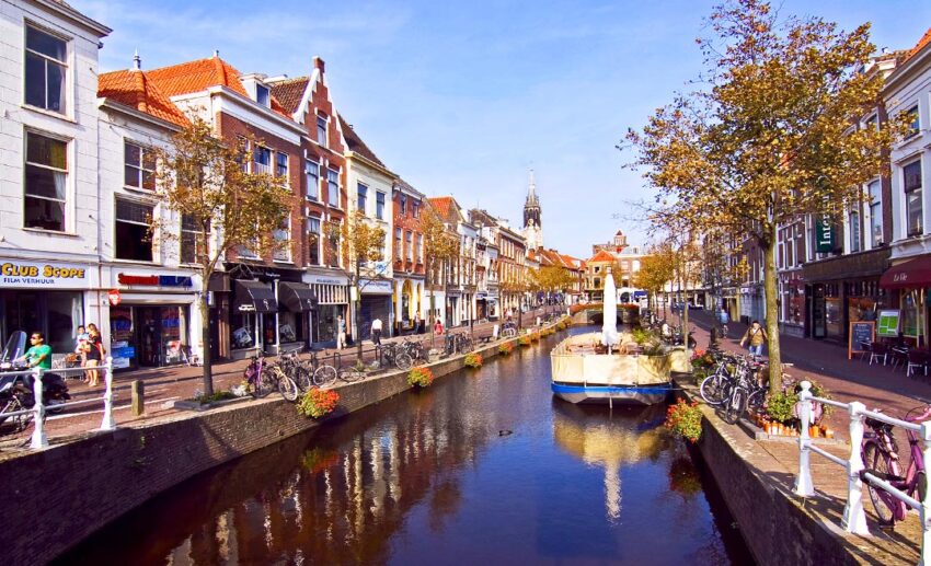 A wide view of an inner-city canal stretching through Delft, with an anchored boat in the foreground and historic brick houses lining the water.