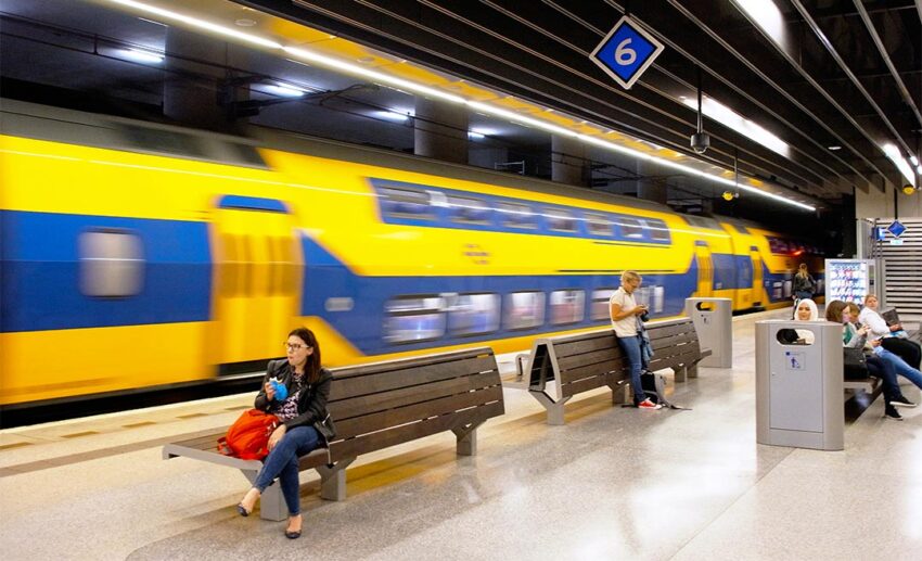 A yellow Dutch commuter train passing through a station, representing the quick and efficient rail link connecting Amsterdam to the heart of Delft.