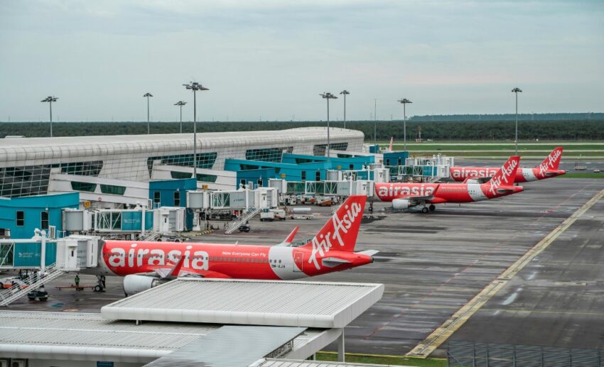 A row of red and white AirAsia airplanes parked at an airport tarmac, representing the participating airlines in the FLYsiswa flight ticket subsidy programme.