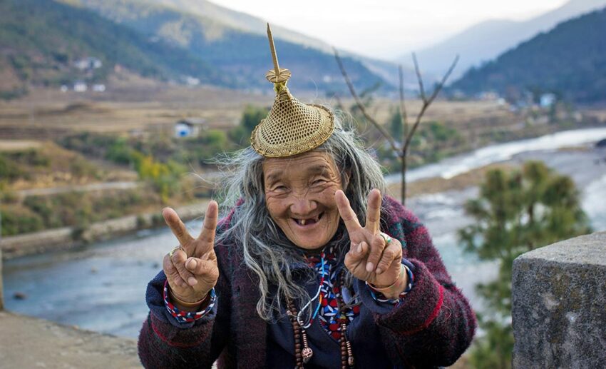 A smiling elderly Bhutanese woman in traditional dress making peace signs in Punakha, Bhutan.