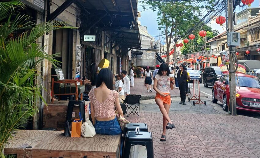 A row of local shops in Bangkok with people walking by on a sunny day.