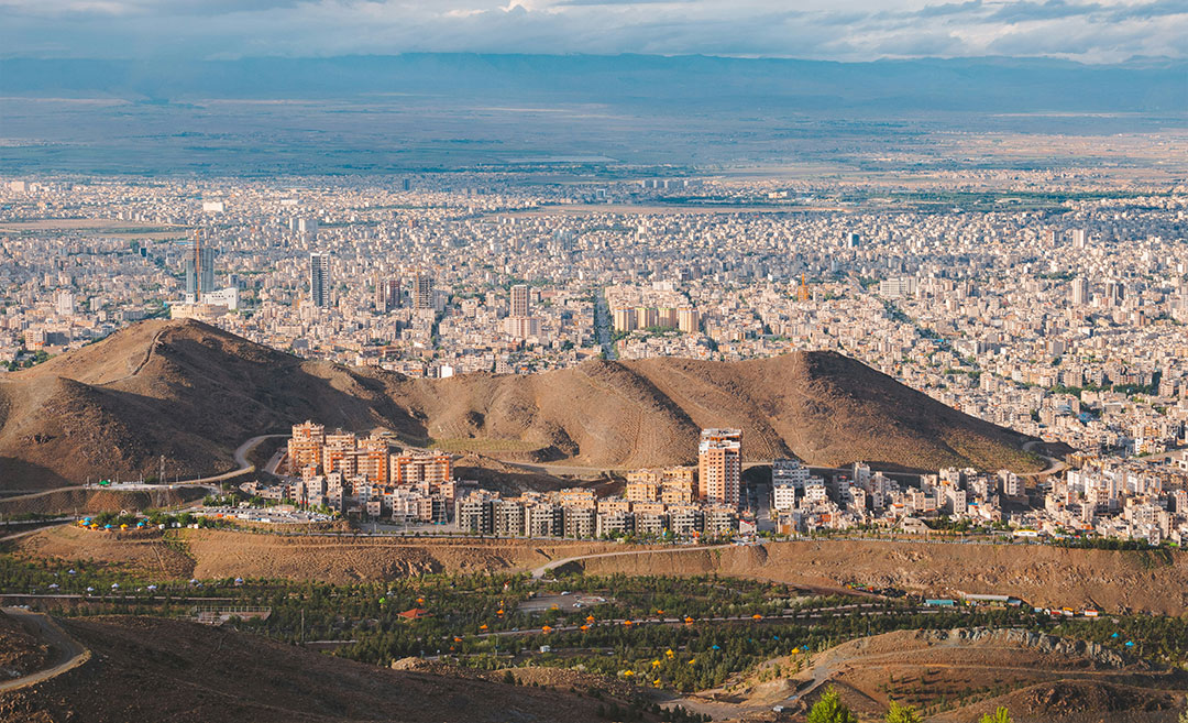 A wide sunset cityscape of downtown Mashhad, Iran, situated in the valley of the Kashaf River between two mountain ranges.
